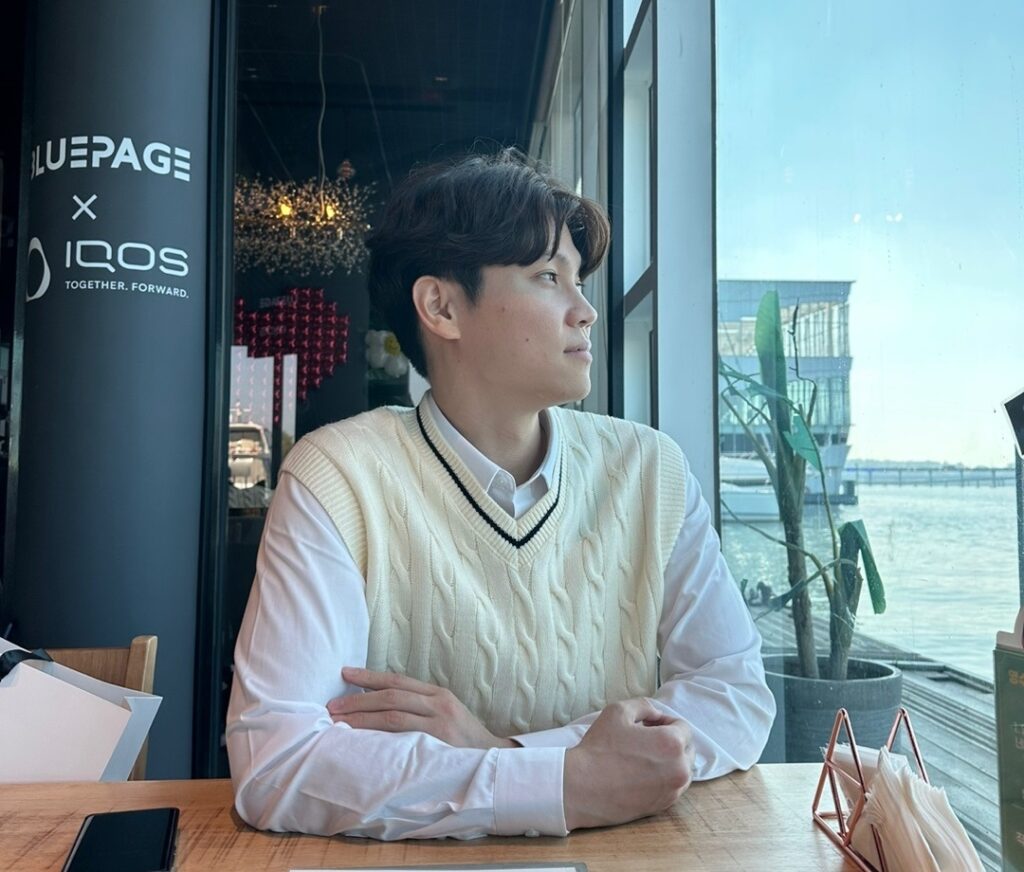 신비버스 창립자 '이서준'이 카페에 물이 보이는 카페에 앉아있다.
날렵하지만 부드럽고 섬세한 외모를 가지고 있다.